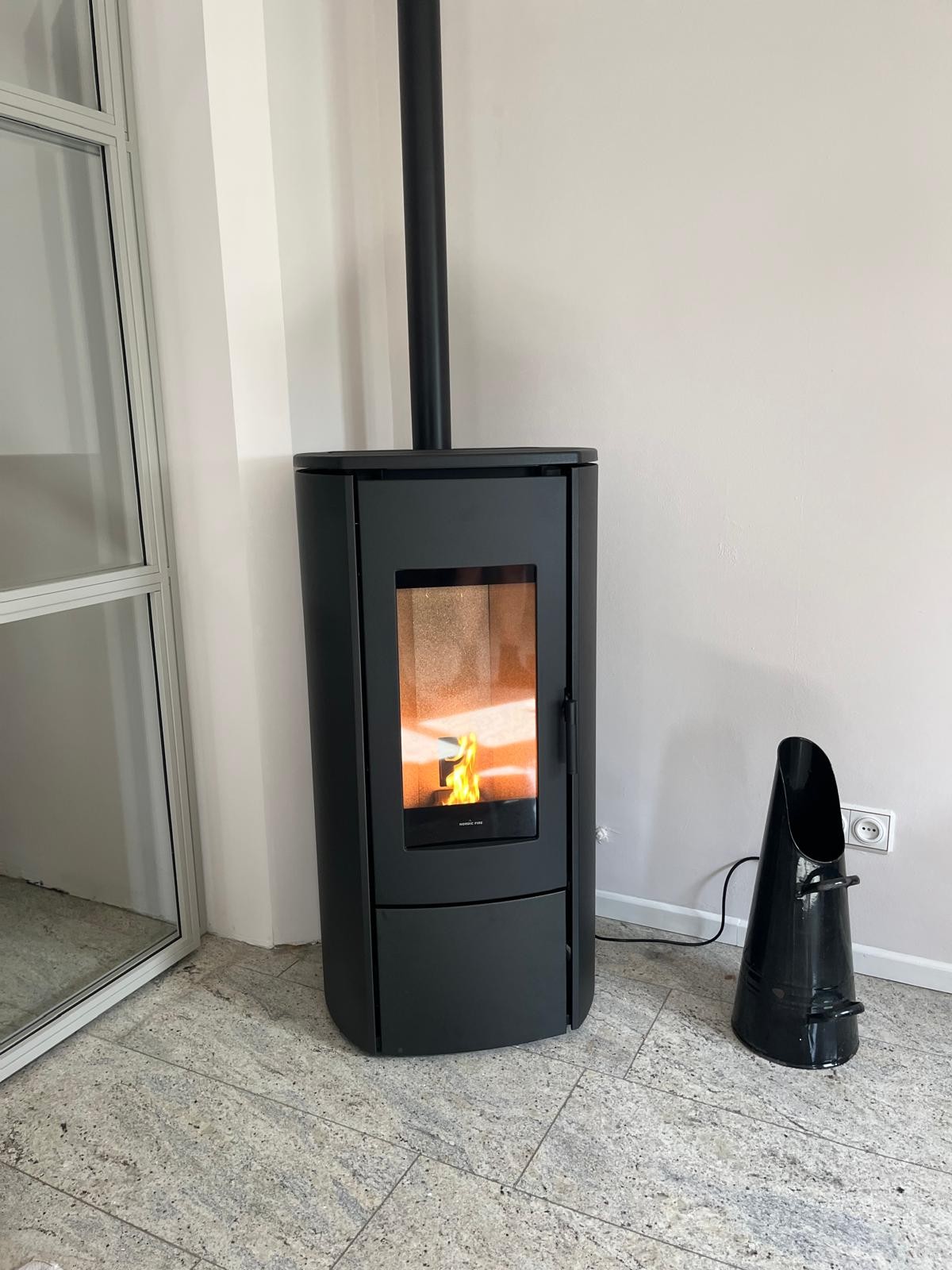 Nordic Fire pelletkachel schuin in een hoek met een kolenkit ernaast.